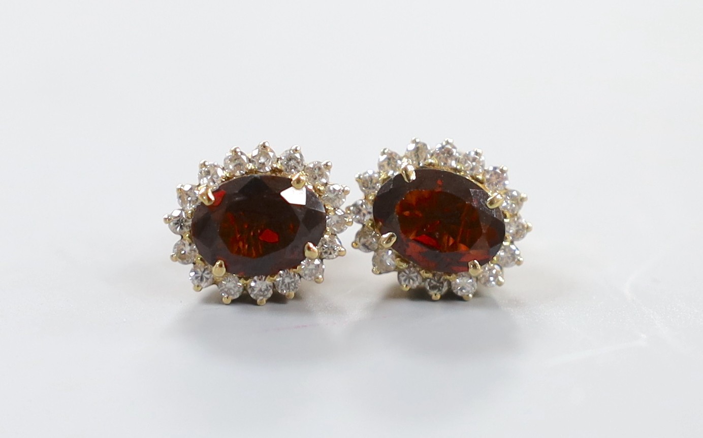 A modern pair of yellow metal, garnet and diamond cluster set oval earrings, 11mm, gross weight 4.8 grams.